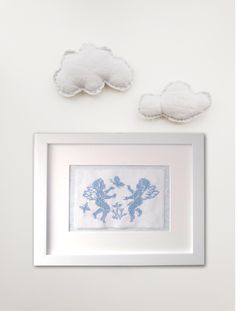 two framed pictures are hanging on the wall next to clouds and a cross - stitch pattern