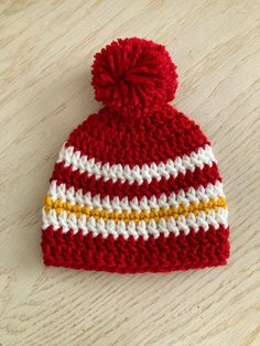 a red and white knitted hat with a yellow stripe on the side sitting on top of a wooden table