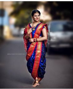 a woman in a blue and red sari walking down the street with her hand on her hip