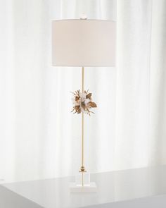 a white lamp sitting on top of a table next to a window with curtains behind it