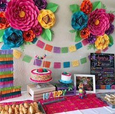 colorful paper flowers decorate the wall above a dessert table