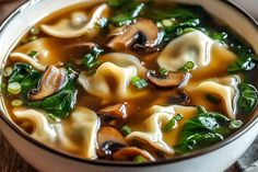 a white bowl filled with pasta and spinach soup on top of a wooden table