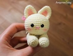 a small crocheted cat sitting on top of a wooden floor next to a person's hand