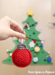 a hand holding a crocheted ornament in front of a christmas tree