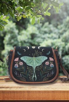 a hand painted purse sitting on top of a wooden table next to a green tree