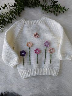 a knitted sweater with flowers on the front and back, sitting on a white furnishing