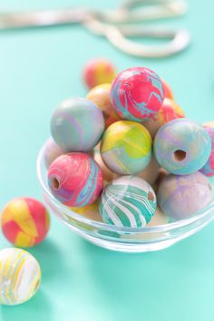 there are many marbles in the bowl on the table next to scissors and thread