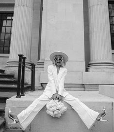 a woman in a white suit and hat sitting on steps