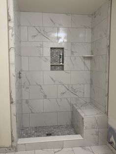 a bathroom with white marble tile and gray grouted floor tiles on the shower wall