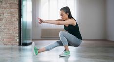 a woman is doing squats in the middle of an empty room with a brick wall