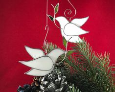 two white stained glass birds hanging from a pine cone on a christmas tree ornament