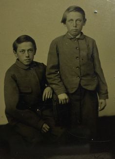 an old black and white photo of two young boys in uniforms, posing for the camera