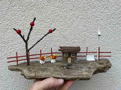 a hand holding a piece of wood with a house on it and flowers in pots