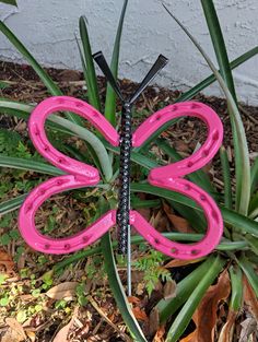 a pink butterfly shaped object sitting on top of green grass next to a plant with leaves