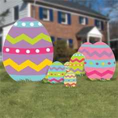 three decorated easter eggs sitting in the grass near a large brick house with blue windows