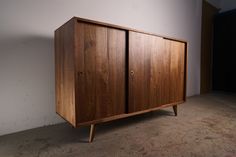 a wooden cabinet sitting on top of a floor next to a white wall in an empty room