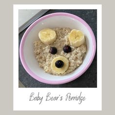 a bowl filled with oatmeal topped with banana slices and blueberries in the shape of a bear's face