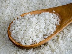 a wooden spoon filled with white rice on top of a bed of sea salt or sugar