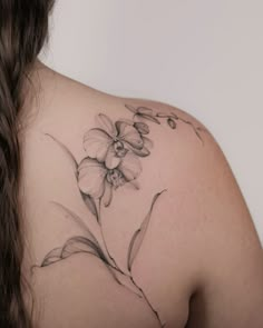 the back of a woman's shoulder with an orchid tattoo on her left shoulder