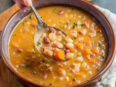 a person holding a spoon full of soup with beans and sausage in a brown bowl