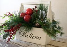 a white box filled with red balls and greenery sitting on top of a wooden table