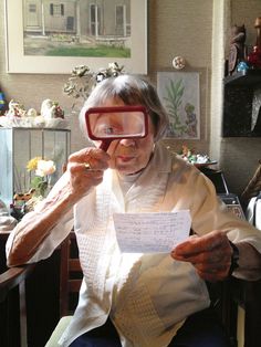 an older woman sitting in a chair looking through a magnifying glass at something