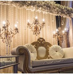 an ornate couch with pillows and chandelier in front of a curtained wall