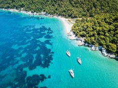 two boats are in the water next to some green trees and an island with white sand