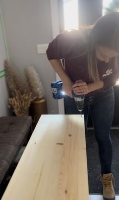 a woman is holding a cup and sanding down the wood on top of a table