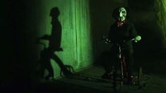 a creepy man riding a bike in the dark with his shadow on the wall behind him