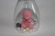 a pink teddy bear sitting in a glass vase filled with pearls and other beads on a white surface