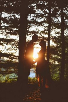 two people standing next to each other in front of trees with the sun behind them