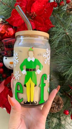 a hand holding up a mason jar with an elf on it and the word elf painted on it