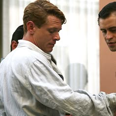 two men standing next to each other in front of a building and one is tying his tie