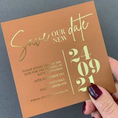 a person holding up a gold foil save - our - date card