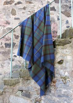 a blue and green tartan plaid blanket hanging on a stair rail next to a stone wall