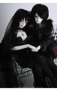 two dolls dressed in gothic clothing sitting on a bench