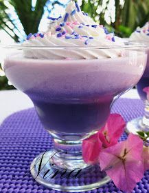 two glasses filled with dessert sitting on top of a purple table cloth next to pink flowers