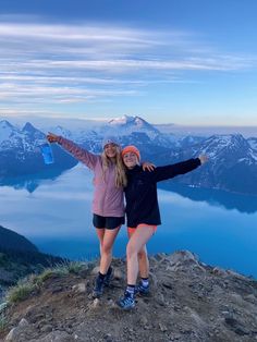 two young women standing on top of a mountain with their arms in the air and one holding a water bottle