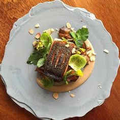 a fish dish on a plate with lettuce, nuts and other toppings