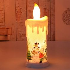 a lit candle with snowmen and christmas trees on it, sitting on a table