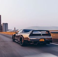 a silver sports car driving down the road with tall buildings in the backgroud