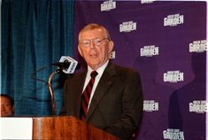 a man in a suit and tie standing at a podium with a microphone behind him