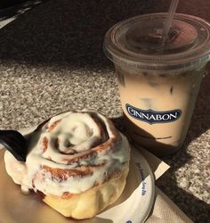 a cinnamon roll sitting on top of a plate next to a cup of coffee with a straw in it