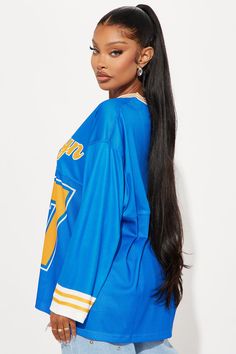 a woman with long black hair wearing a blue hockey jersey and ponytail in front of a white background