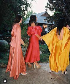 three women in long dresses are standing outside