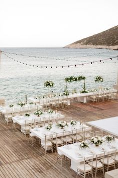 an outdoor wedding setup with tables and chairs on the deck overlooking the ocean in front of string lights