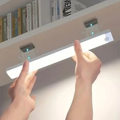 two hands are reaching up to the ceiling light in front of bookshelves and shelves