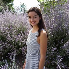 a woman standing in front of purple flowers and lavender bushes with her hands in her pockets