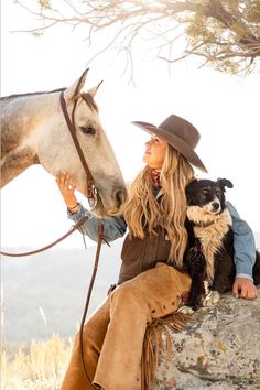 a woman sitting on top of a rock next to a horse and holding a dog